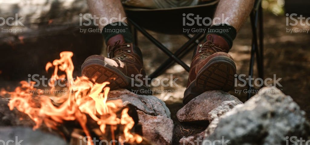 cropped picture of old man’s feet held up to a campfire