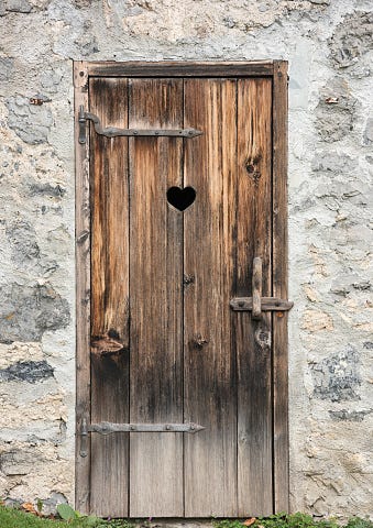 Uma foto da porta de um banheiro com um coração cortado na madeira