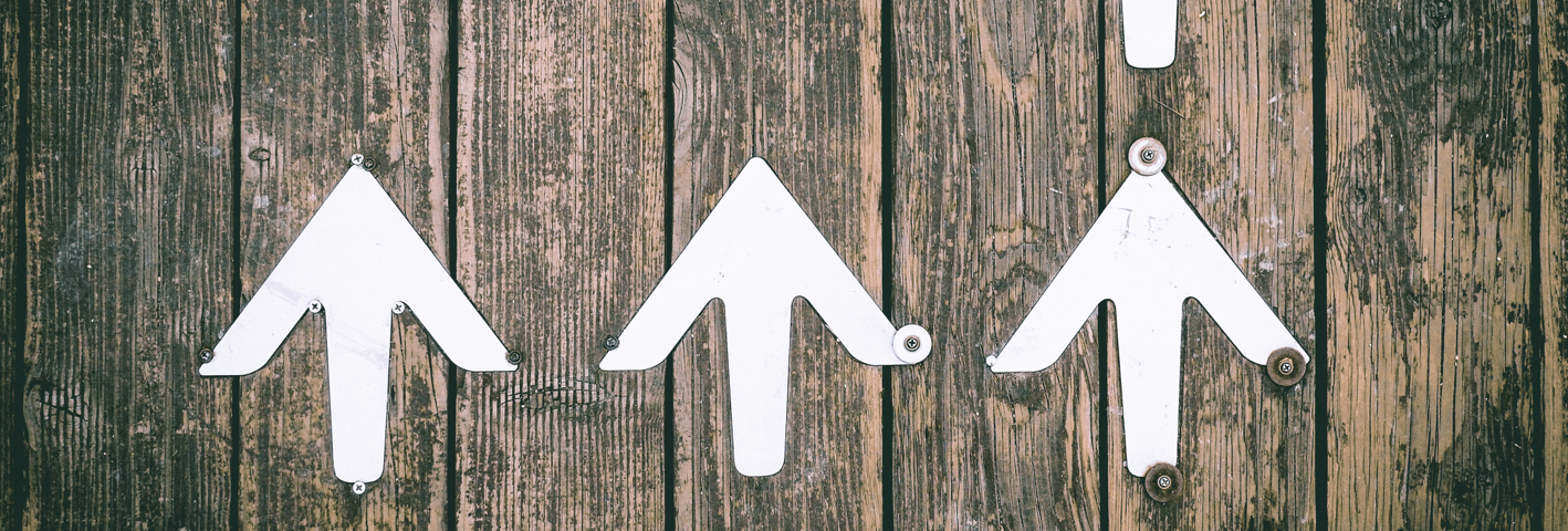 Three white arrows on a wooden background pointing up.