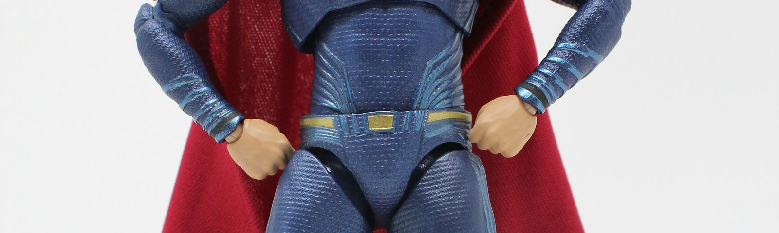 Toy figure of superman in blue suit and a red cape and red boots with an S on his chest.