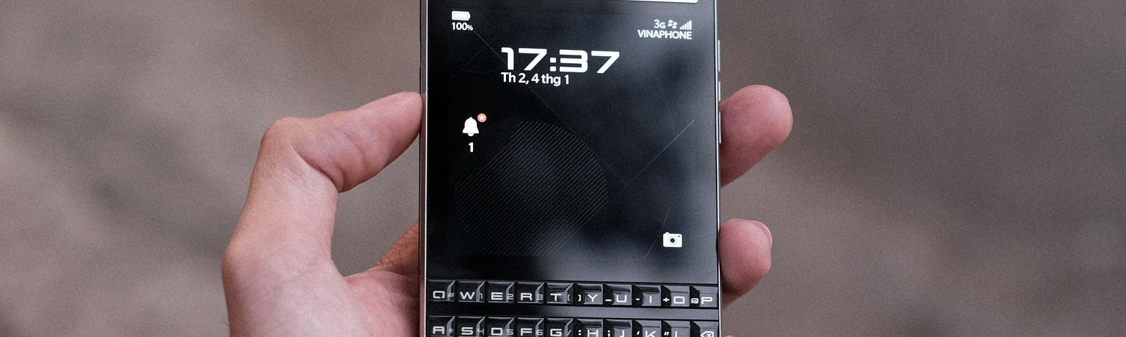 An open hand holds an old BlackBerry smartphone with a physical qwerty keyboard