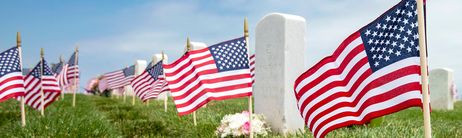 A color photo shows a row of white marble military-style headstones, each decorated with a miniature U.S. flag sticking out of the ground in front of it.