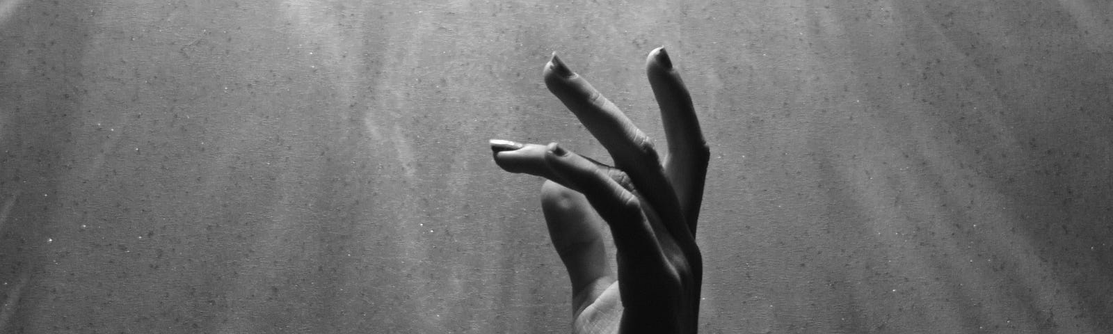 black and white picture of a woman’s hands floating under water- you can see light streaming down