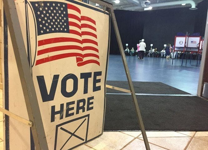 A picture of a polling place with a voting booth in the foreground.