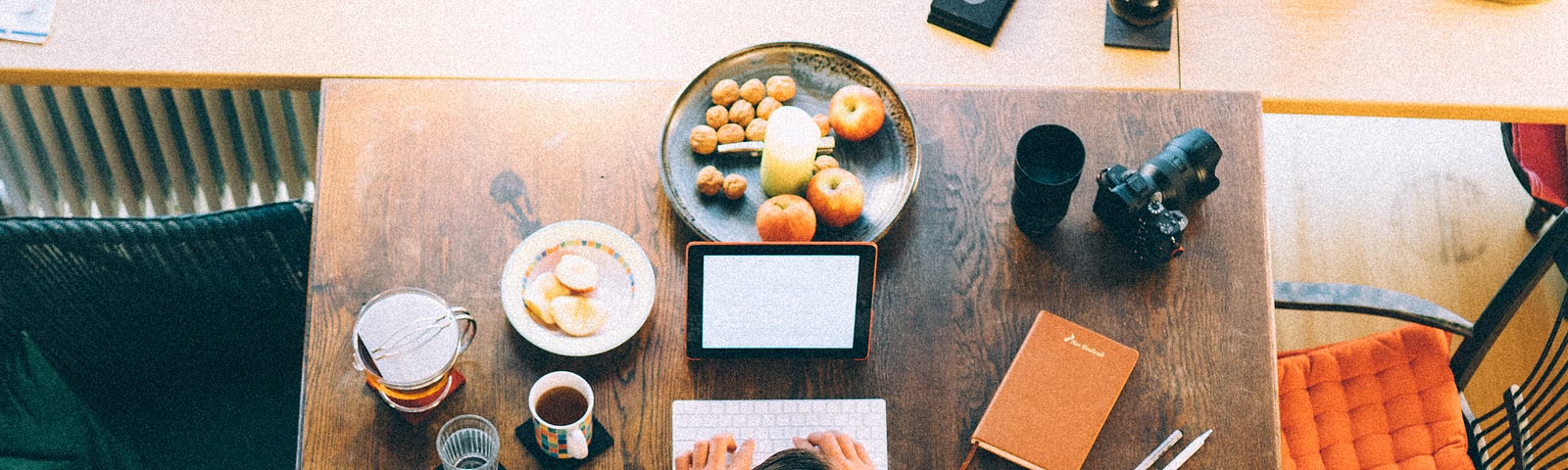 Man types on an iPad on his desk while surrounded by food.