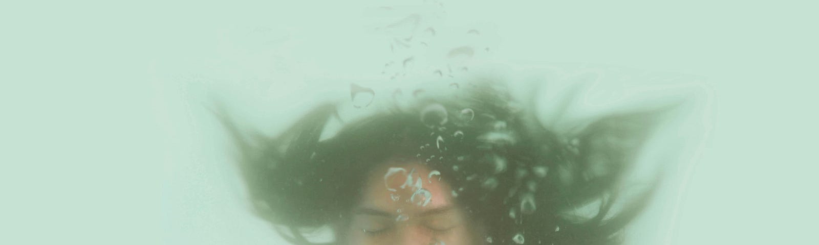 A woman underwater, blowing air from her mouth. Her hair is floating upwards.