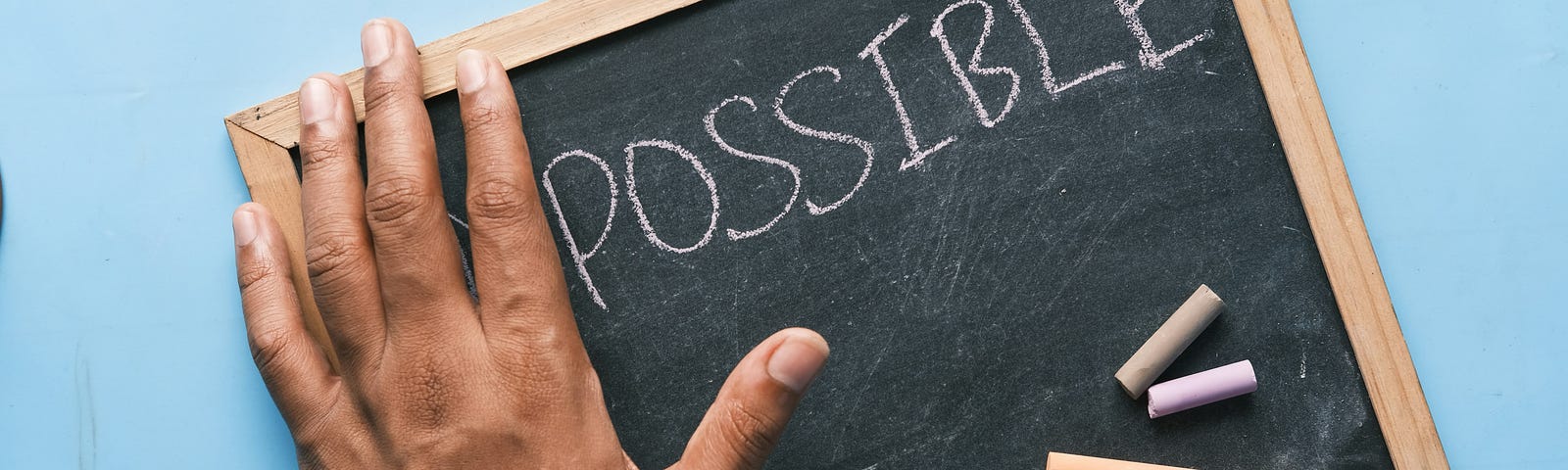 the word “impossible” on a chalkboard, and a hand hiding the “im” to make it look like it says “possible”.