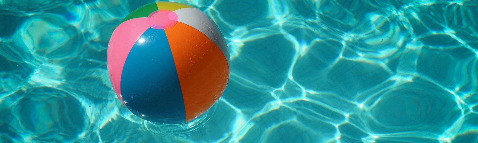 A turquoise swimming pool with a red, blue and gray beach ball in it