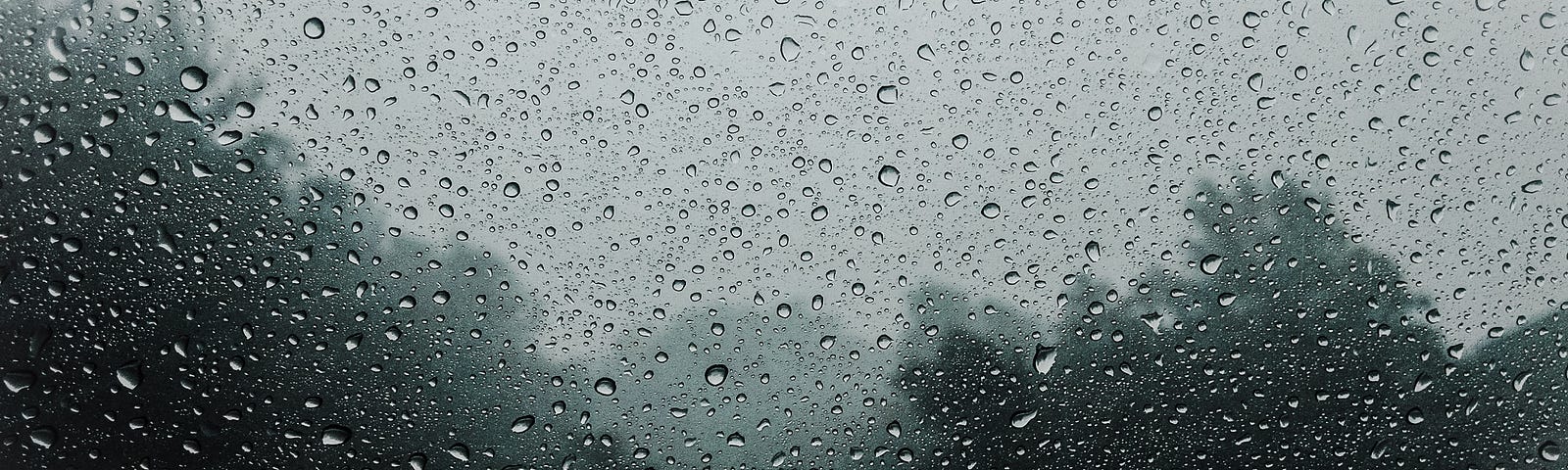 Rain on a window, gray sky and trees beyond