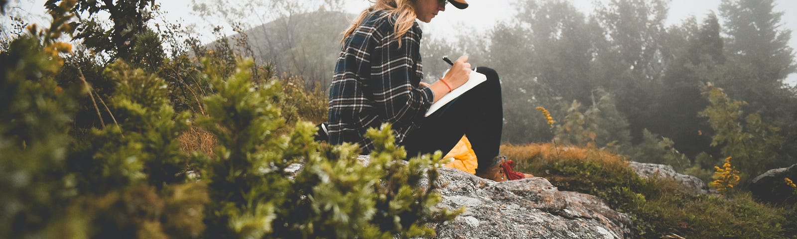 A woman sitting outside in nature and writing.