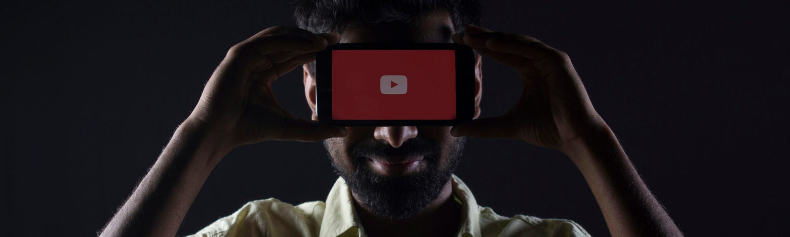 Man hiding his face behind a phone with a red screen and white ‘play’ button.