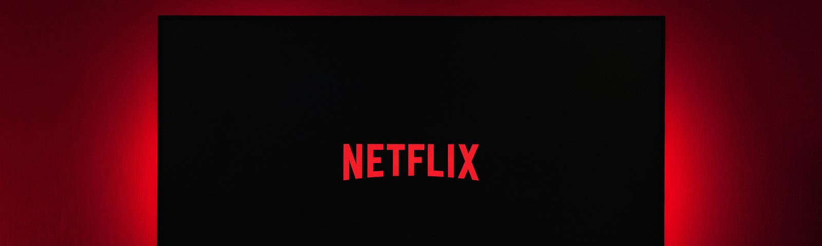 A flat screen television with the word NETFLIX on its screen Red background.