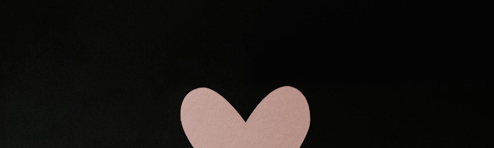 An image of a pink paper heart on a wooden stick against a black background.