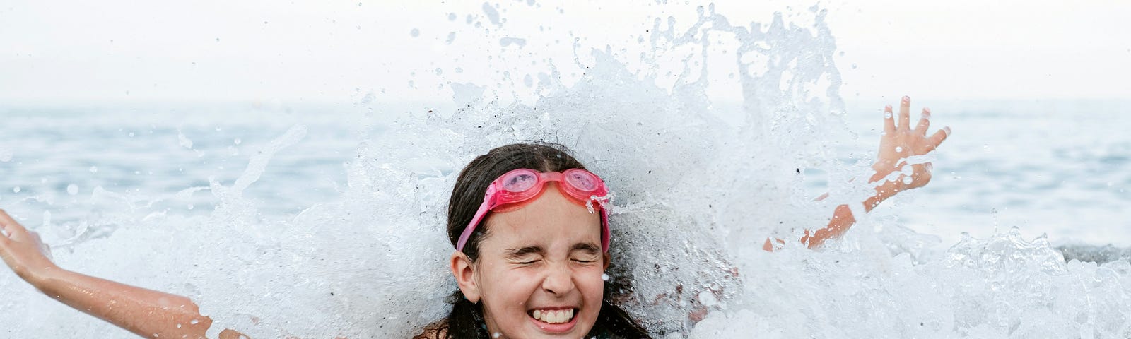 Little girl splashing on the shore with a happy expression on her face, arms spread out