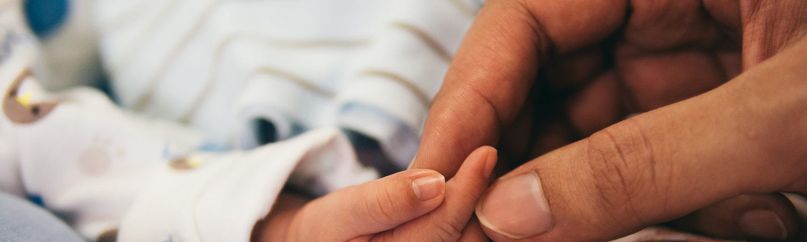 Photo of an adult’s hand holding a baby’s hand.