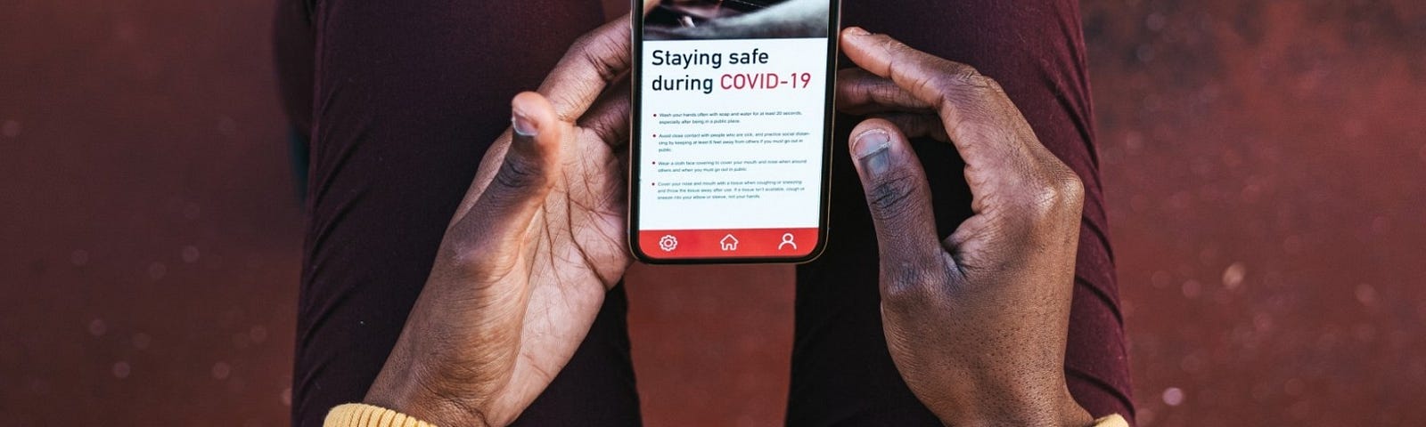 Topdown view of older Black woman holding a cellphone with a news article about COVID-19 on the screen. Photo by LeoPatrizi/Getty Images