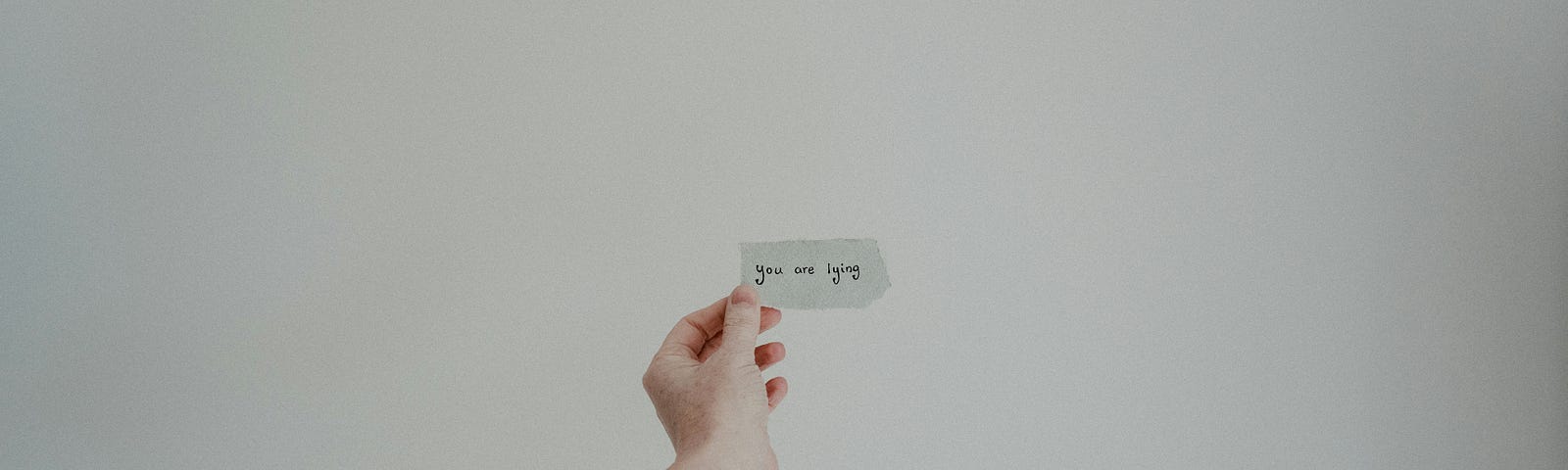 A woman holding a small piece of paper reading “You are lying”