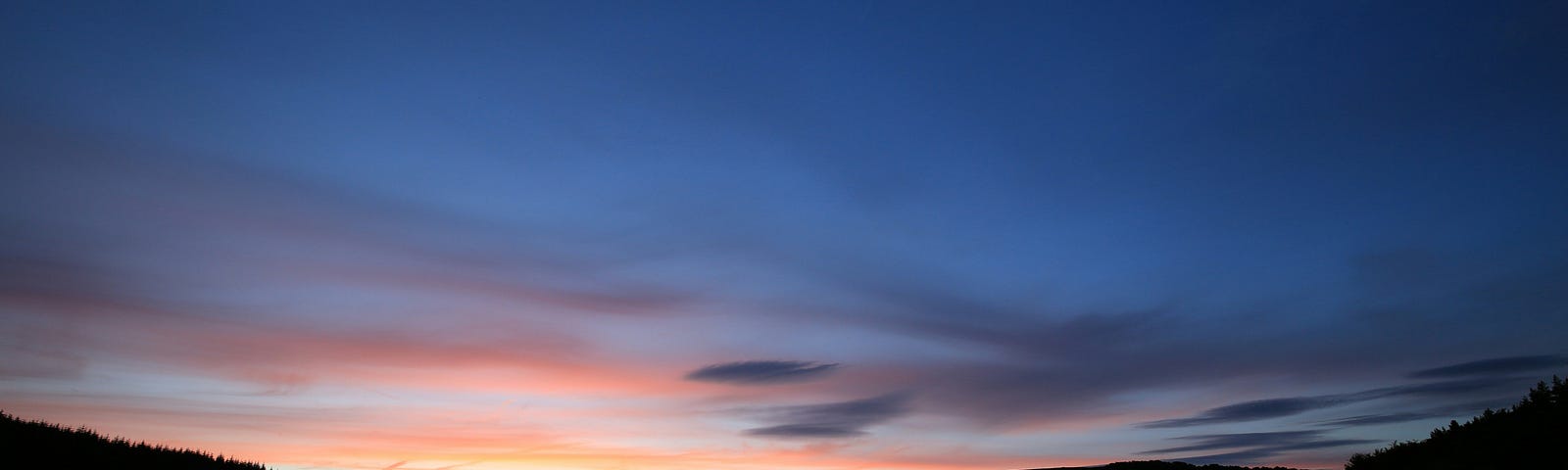 sunset with gentle hills rising on either side of a lake reflecting the fading light of the evening sky