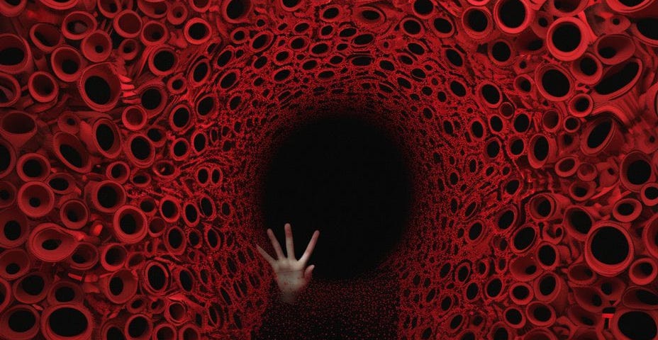 it almost seems like the inside of a uterus, the blood lining, red circles surrounding the inside, where a dark shadow figure holds out one hand in a “stop” motion