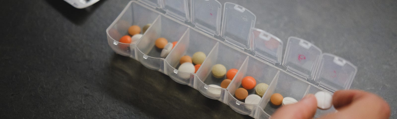 photo of a hand placing a pill into a plastic weekly pill organizer.