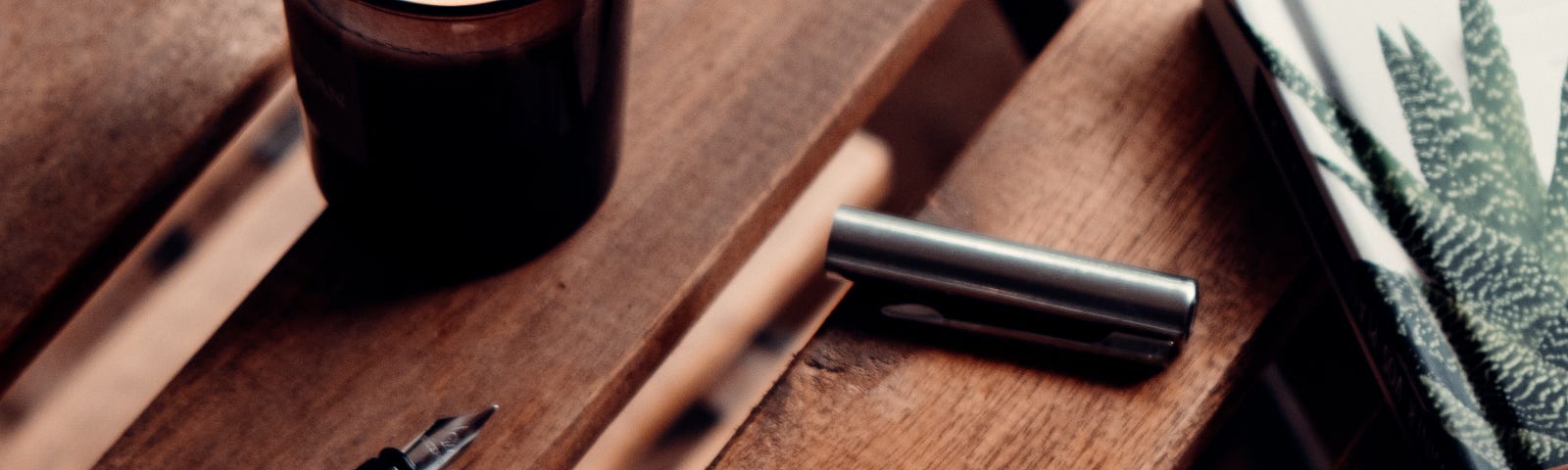 A lit candle, an open pen and a postcard sit on a slatted table.