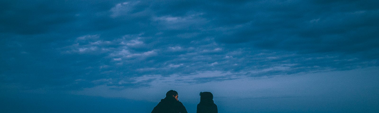 A couple sits at the end of a peer, with midnight blue skies around them.