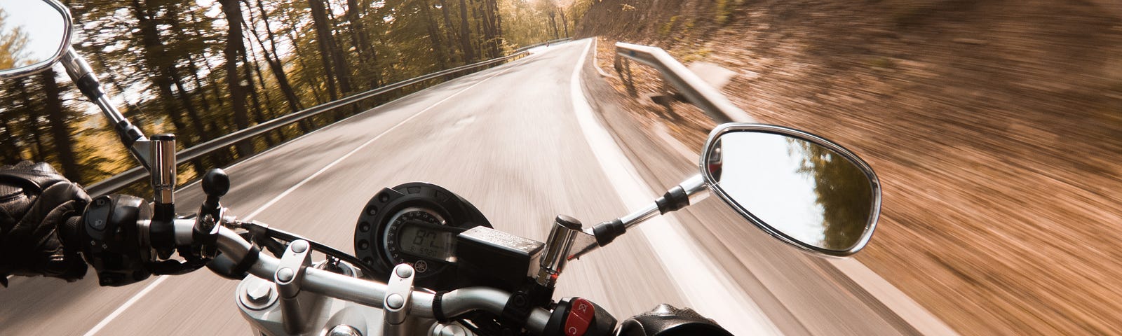 A black motorcycle from the rider’s point of view leaning to the right on a fast mountain road