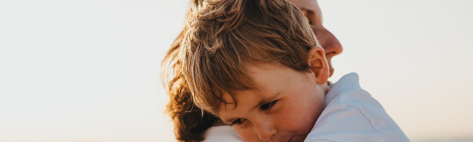 On the sand of a beach somewhere, a mother holds her baby boy gently in her arms.