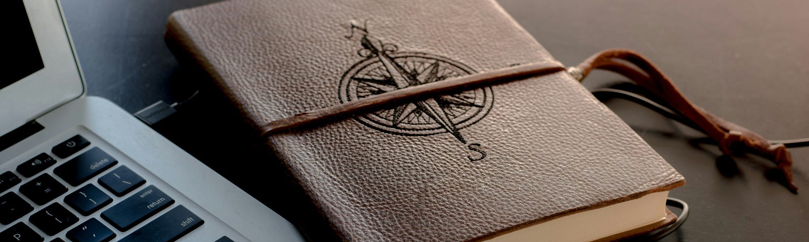 A leather journal with a picture of a compass, notebook, and two pens.