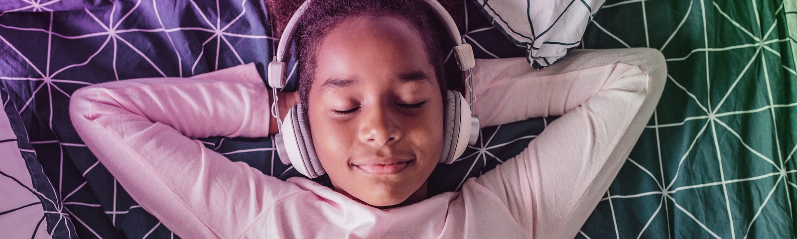 Photo of a middle school girl lying down with her hands behind her head, eyes closed, with headphones on.