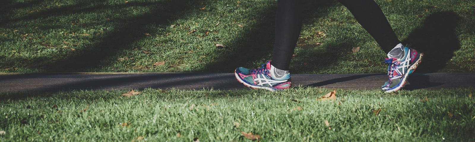 A person walking along a pathway. Only their legs are on view. They are wearing trainers and black leggings. There is grass in the foreground.