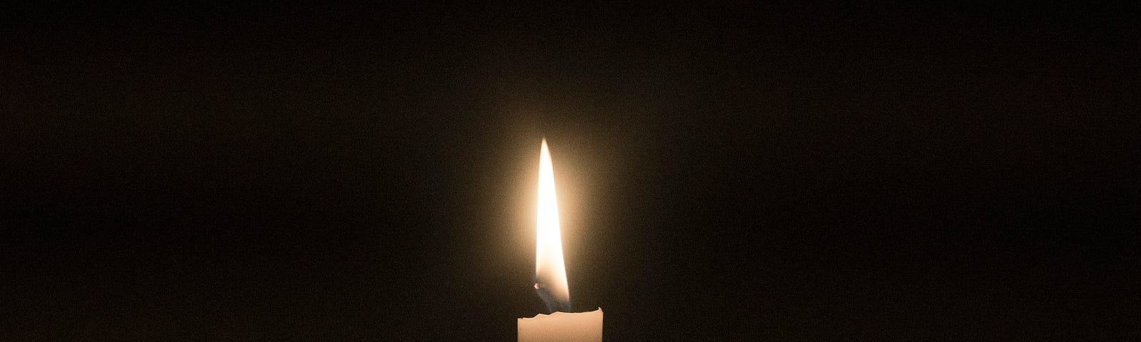 A single thin white candle burns in front of a black background.