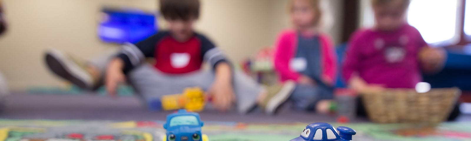 Three small children at daycare sitting on a rug playing with cars.