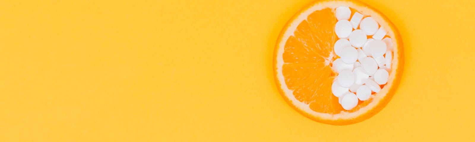 A sliced orange is perched on the upper right of a yellow background. The left of the orange is as expected while the right side is filled with white pills. Recent data suggests vitamin D supplementation lowers the risk of autoimmune diseases.