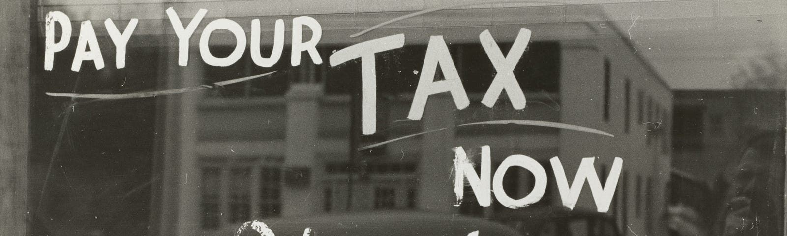 Pay your tax now here, a vintage sign painted on a window.