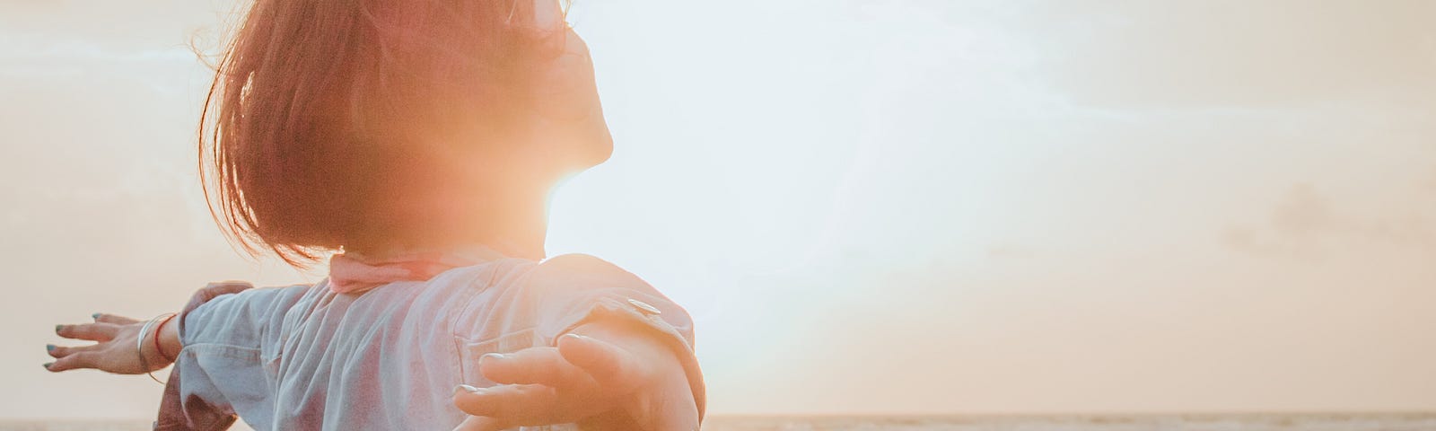 A woman with her arms out stretched towards the ocean.