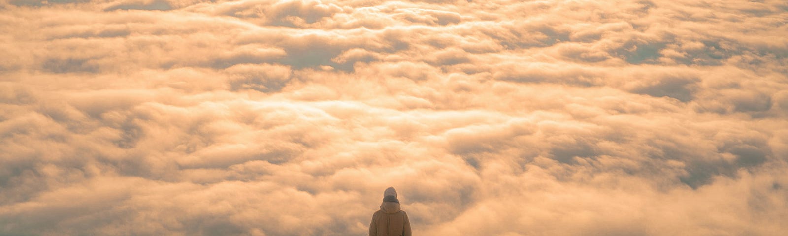 man standing on moutaintop, looking down at clouds.