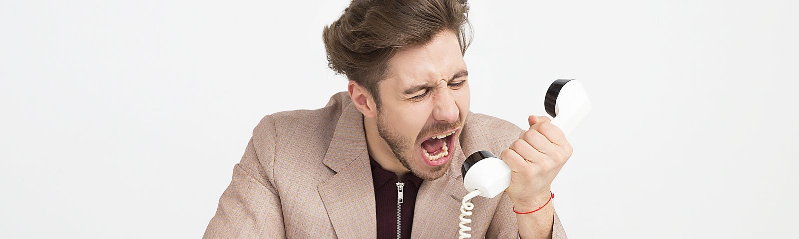 a person screaming into a telephone receiver. the telephone is lying on a surface in front of the person as are a pair of glasses