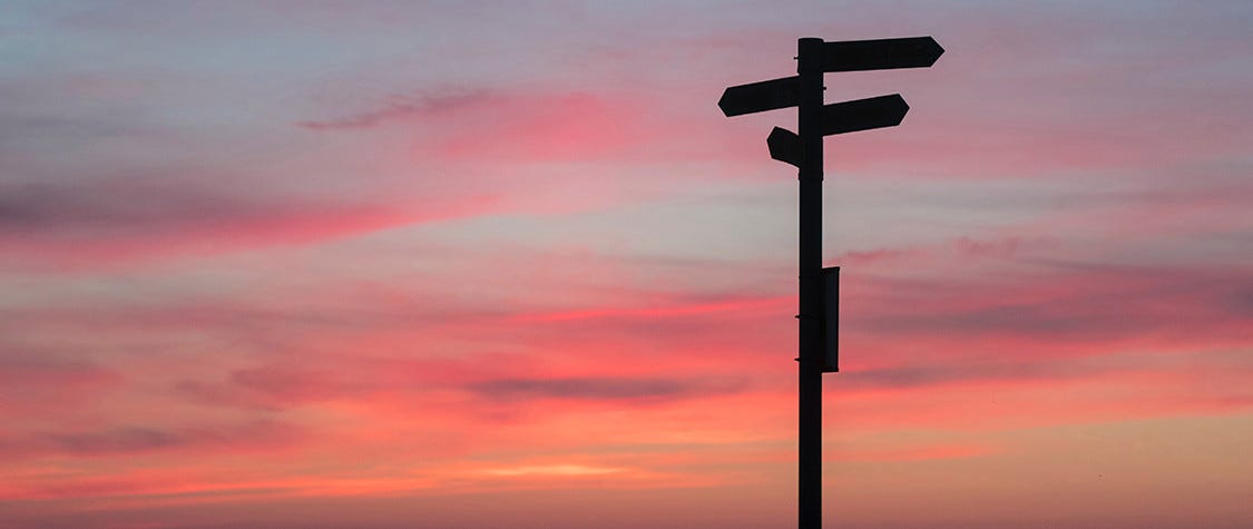 Street signs with a sunset in the distance.