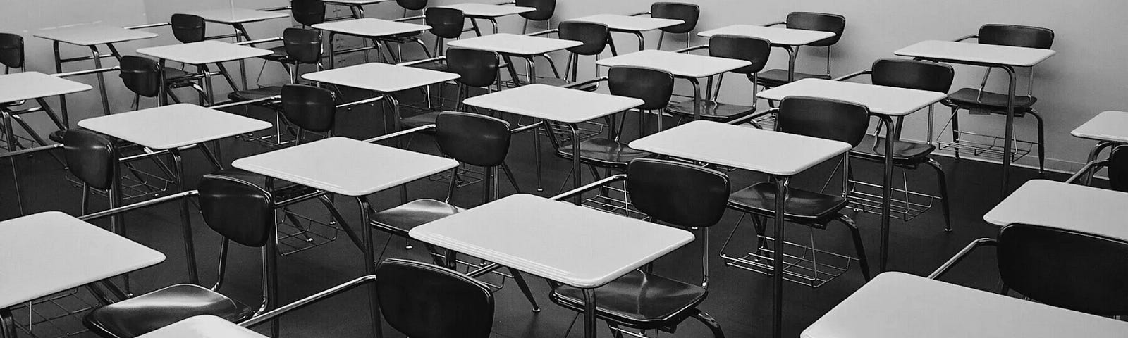 A black and white photograph showing a wide-angle view of a classroom full of student chairs with the wrap around desks.