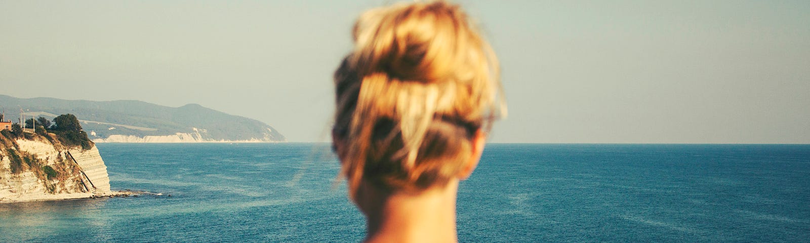 A female torso shown from the back looking out at a seascape.