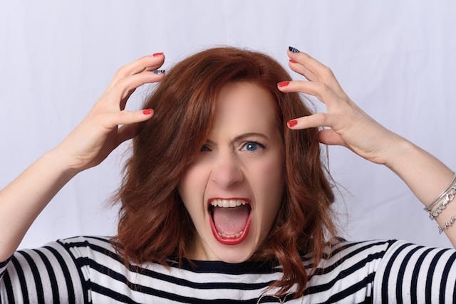 A frustrated woman screaming with her hands held to her head.