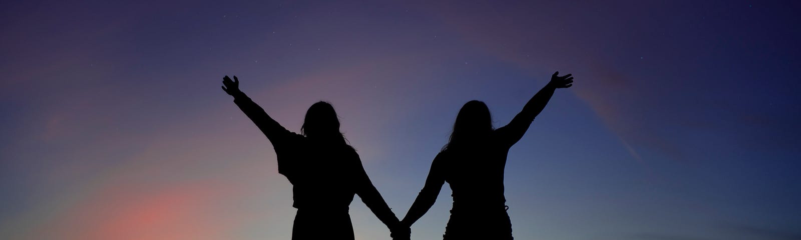 two silhouettes holding hands and standing on a hill with a sunset in the background