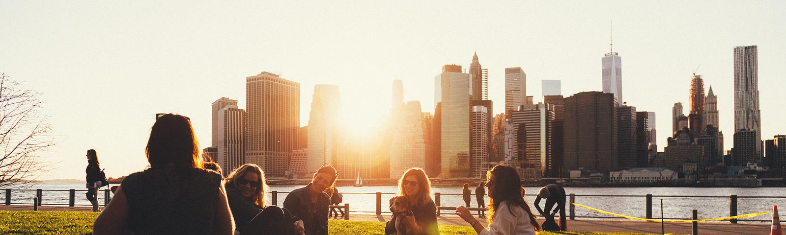 A group of mothers sitting together in a park. A city skyline and sunset are in the background.