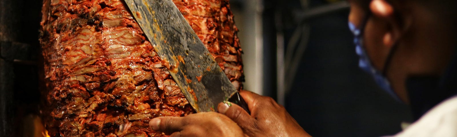 Chef using a large knife to carve al pastor, a seasoned marinated pork.