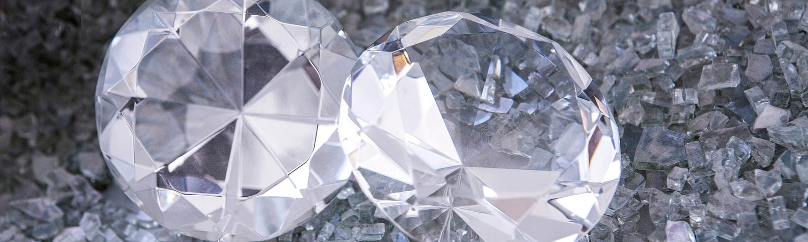 Two clear diamonds are sitting on a pile of broken glass.