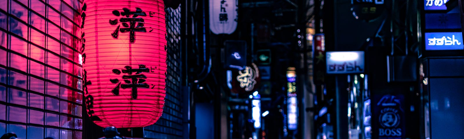 At night, a back alley in downtown Tokyo is lit by business signs