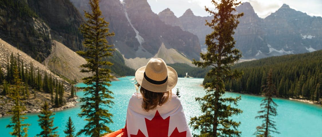 Woman facing a lake with a Canadian flag draped across her back.