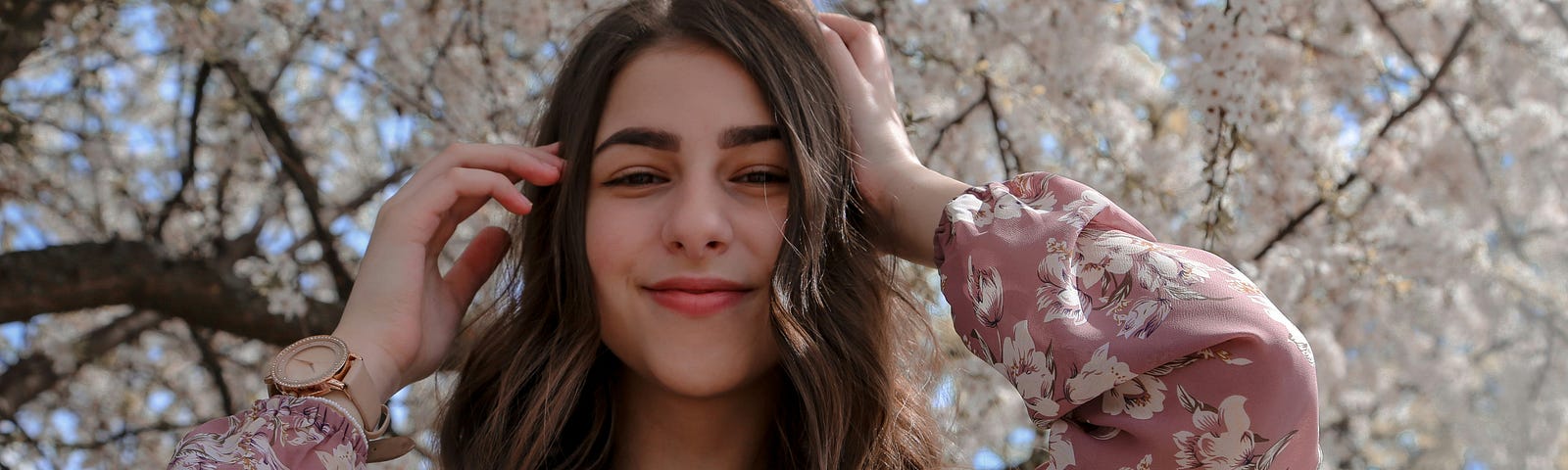 A woman smiles under a cherry blossom tree