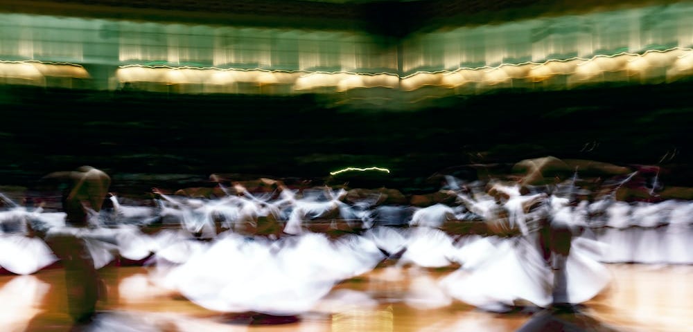 Picture shows many Sufi dervishes dressed in white whirling enraptured in their own bliss